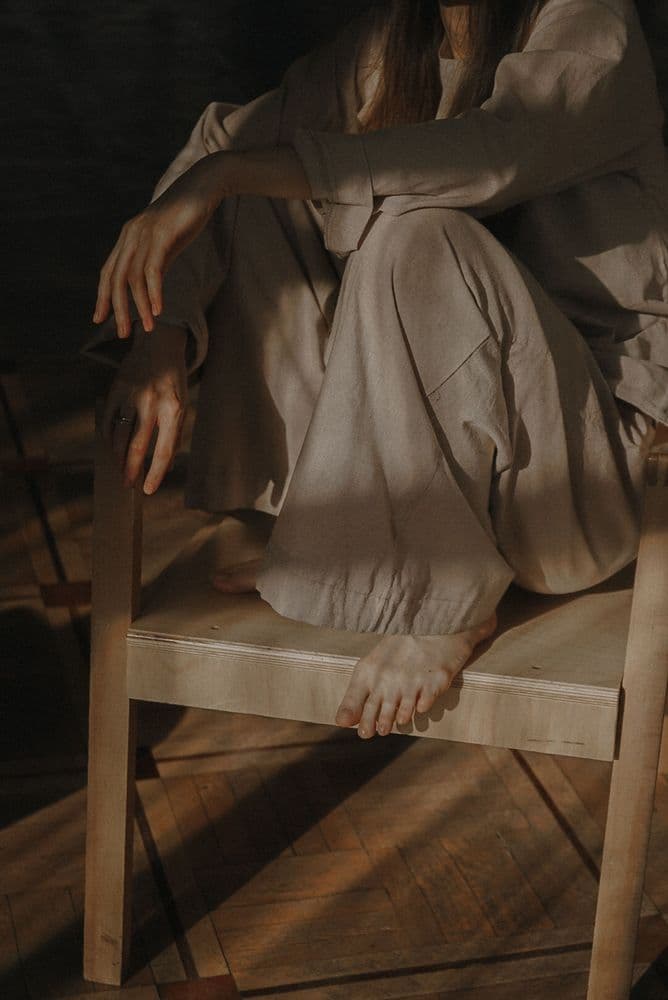 Someone in brown linen resting on a wooden chair in warm light
