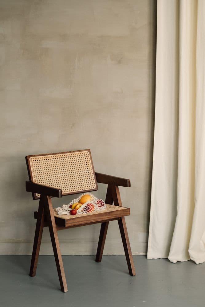 A cane chair holding a net bag of fruit beside a linen curtain