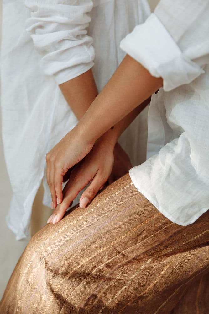 Hands resting on a rust linen skirt and a white shirt